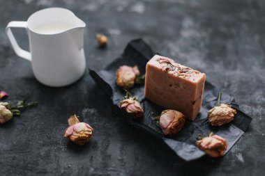 Ev yapımı çiçek sabunu. Koyu arkaplanda doğal sabun ve gül çiçekleri. Spa konsepti, vücut bakım ürünleri. Düz yatış, üst görünüm