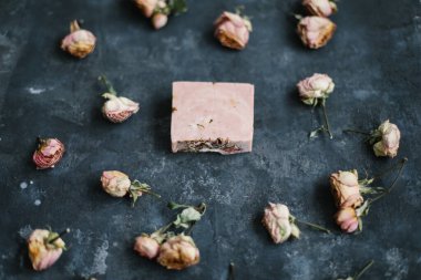 Ev yapımı çiçek sabunu. Karanlık arka planda doğal sabun ve çiçekler. Spa konsepti, doğal kozmetik. Düz yatış, üst görünüm