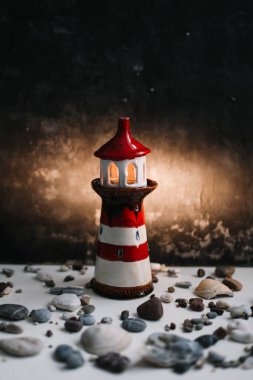 Koyu arkaplanda deniz kabukları ve taşlar olan küçük dekoratif deniz feneri. Yaz, tatiller, tatil konsepti. Düz yatış, üst görünüm