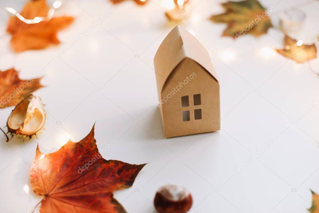 Cozy autumn composition. Paper house surrounded by autumn leaves on a white table. Greeting card, Fall, Thanksgiving concept.