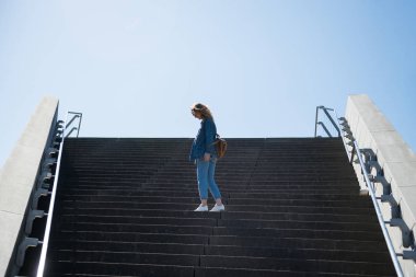side view of woman standing on steps with blue sky on background in copenhagen, denmark clipart