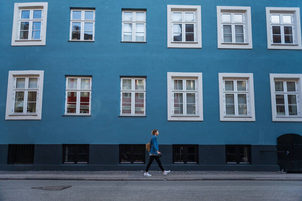 side view of young woman walking near blue house with large windows in copenhagen, denmark