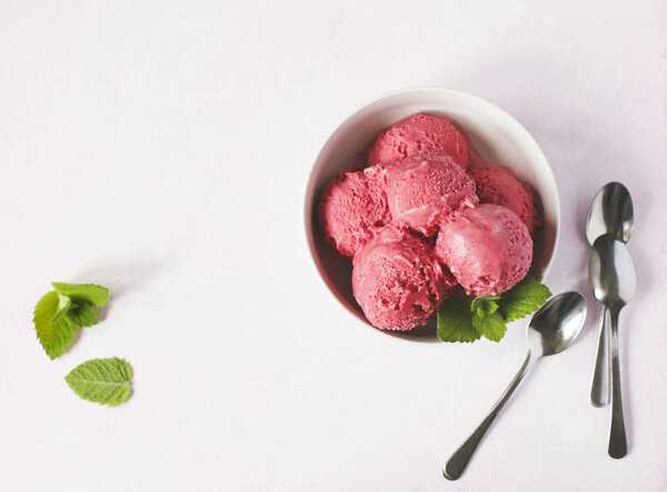 Raspberry ice cream in white bowl on light pink background, top view