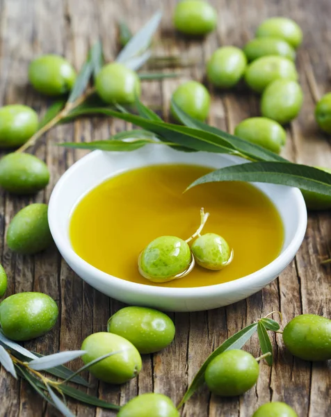 Fresh green olives with leaves and olive oil on wooden background