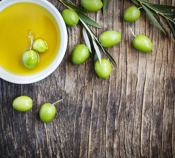 Fresh green olives with leaves and olive oil on wooden background with copy space