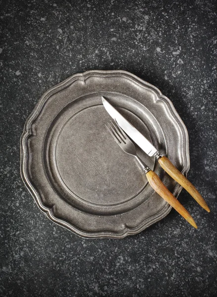 Vintage empty plate and fork and knife on dark grey stone backgr — Stock Photo, Image