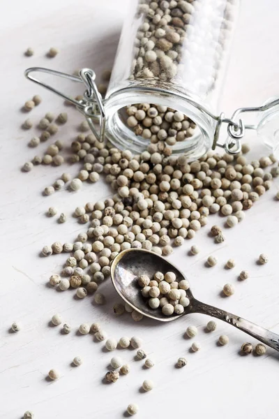 Pimentos brancos em jarra e colher no fundo branco — Fotografia de Stock