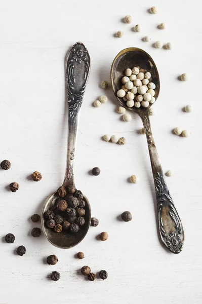 White and black peppers in spoons — Stock Photo, Image