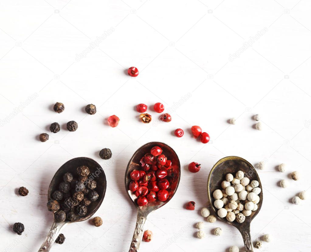 Pink, White and black peppers in spoons, top view