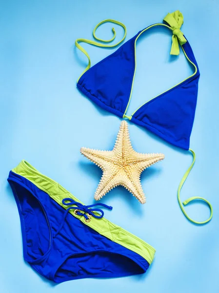 Blue swimsuit and starfish on blue background, top view. — Stock Photo, Image