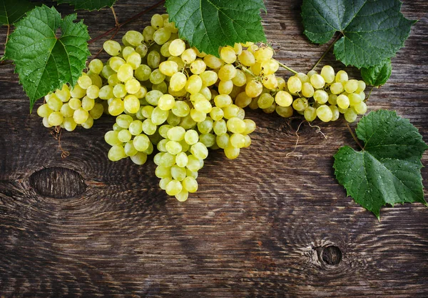 Frische reife Trauben mit Blättern auf einem hölzernen Hintergrund. — Stockfoto