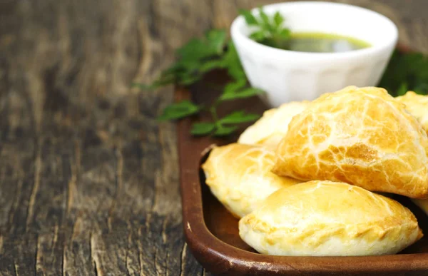 Empanadas z sosem Chimichurri na drewnianym stole — Zdjęcie stockowe