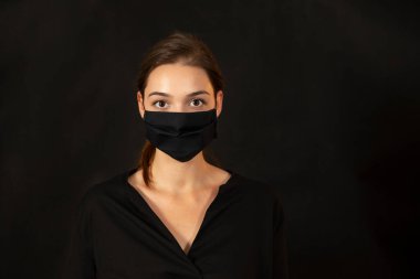 Karanlık arka planda maske takan genç bir kadının stüdyo portresi..