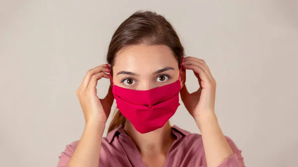 Young female nurse putting on a red fabric medical mask during pandemic. — Stock Photo, Image