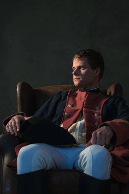 Sandalyede oturan diz şapkası olan tarihsel İmparatorluğu adam. Bir kenara arıyorsunuz.