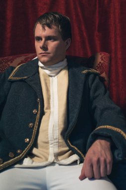 Tarihsel regency adam kırmızı perde önünde oturur.