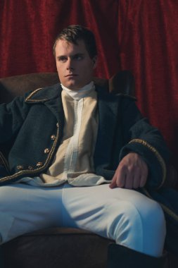 Ciddi tarihsel regency adam kırmızı perde önünde oturur.