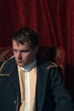 Tarihsel regency adam kırmızı perde önünde oturur.