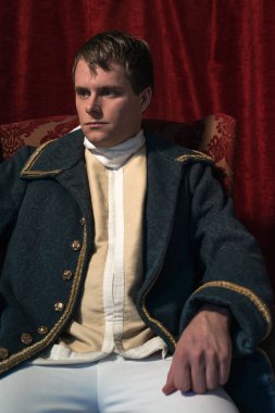 Tarihsel regency adam kırmızı perde önünde oturur.