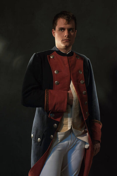 Serious historical regency man holds hand in jacket.