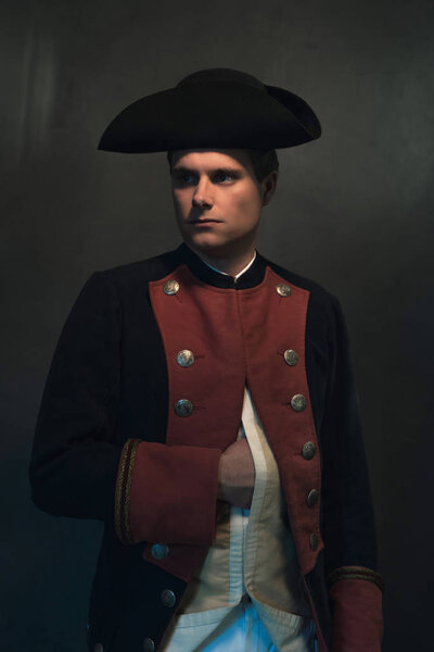 Historical regency man in hat holds hand in jacket.