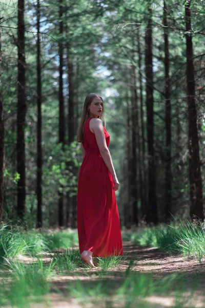 穿红色连衣裙的金发女郎在森林小路上看着肩膀 — 图库照片