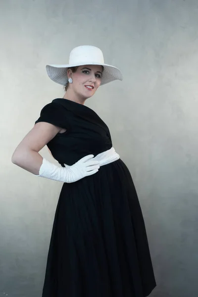 白い帽子と黒いドレスでレトロな 1950 年代の妊娠中の女性の笑みを浮かべてください カメラに向かっています — ストック写真
