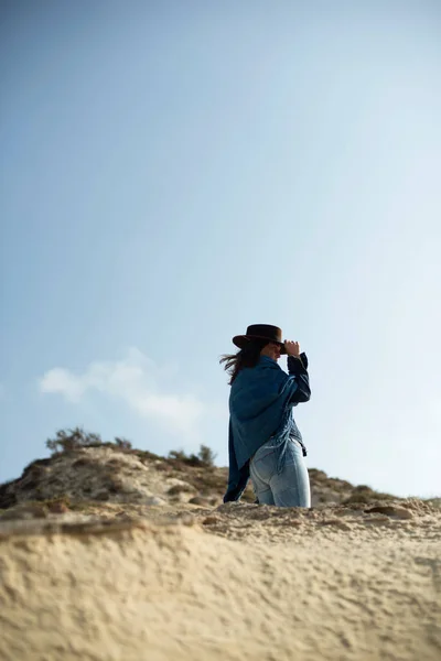 青い布と風の荒涼とした風景の中の茶色の帽子立っているブルネットの女性 — ストック写真