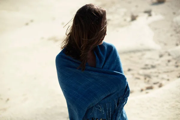 Brunette woman in blue cloth standing in desolate windy landscape. Rear view.