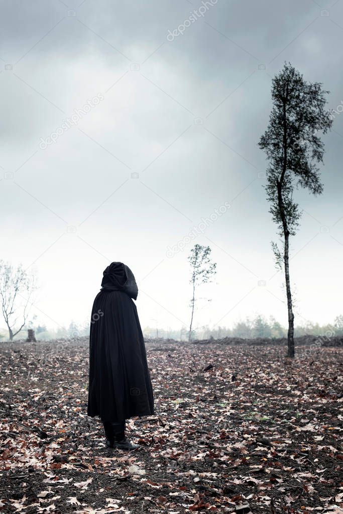 Woman in black cape in moody landscape.