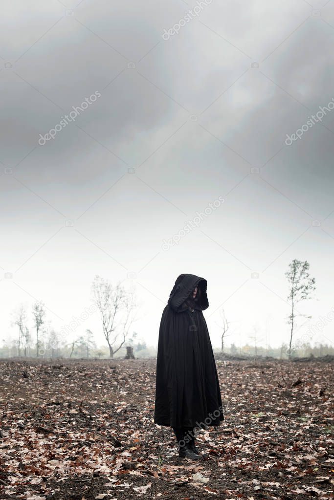 Woman in black cape in moody landscape.