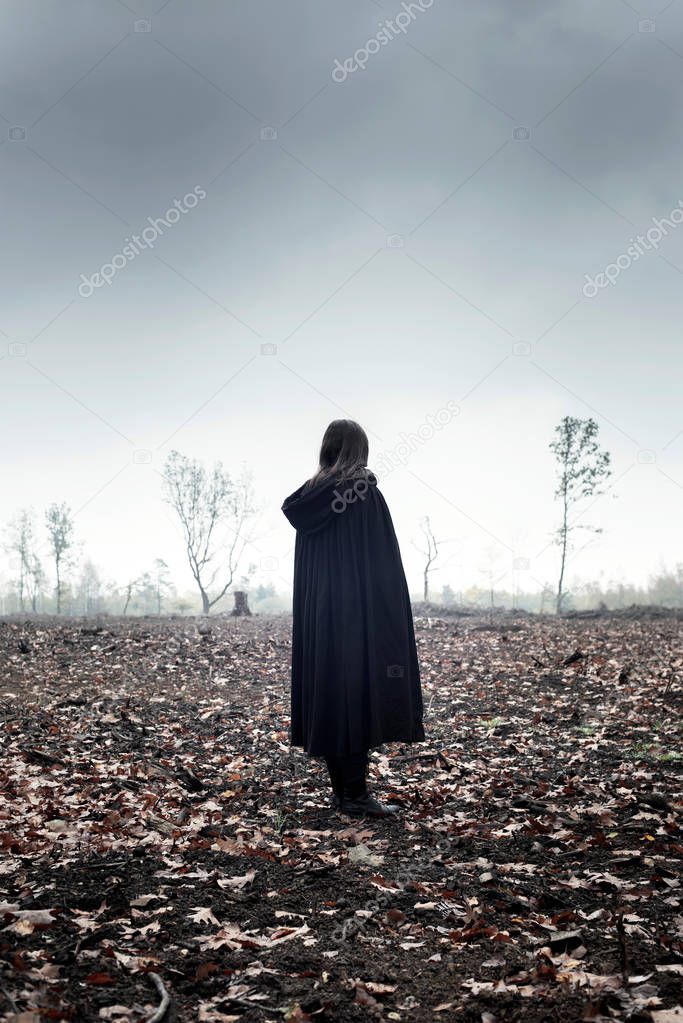 Woman in black cape in moody countryside.