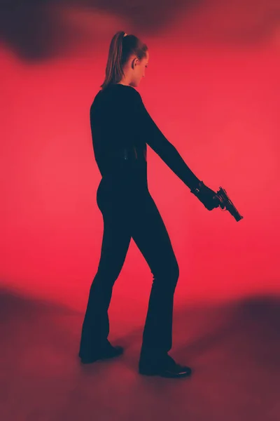Силуэт женщины в черном, держащей пистолет. Против красного бэкгро — стоковое фото