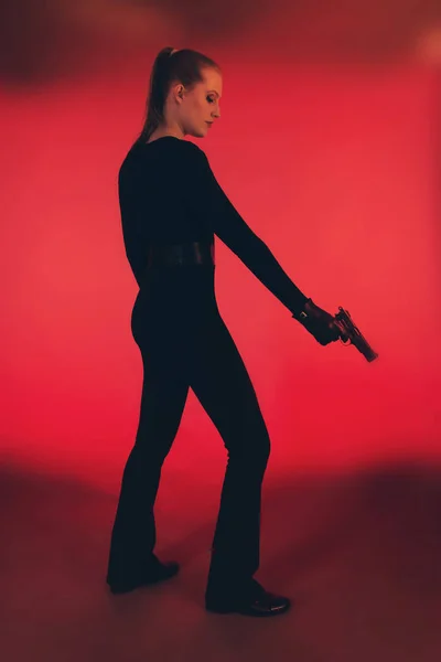 Силуэт женщины в черном, держащей пистолет. Против красного бэкгро — стоковое фото