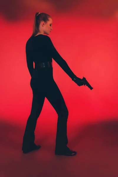 黑色手持手枪的妇女剪影。反对红色的背板 — 图库照片