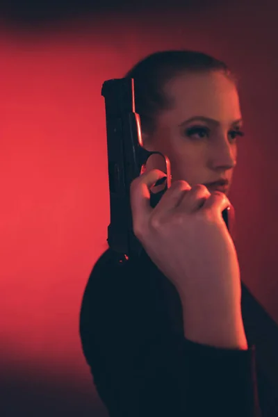 Блондинка с пистолетом на красном фоне . — стоковое фото