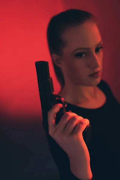 Blonde woman with pistol against red background. — Stock Photo, Image