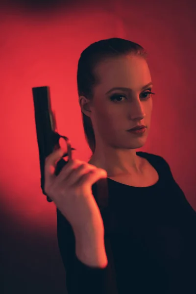 Blonde vrouw met pistool tegen rode achtergrond. — Stockfoto