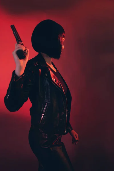 Femme avec arme habillée en noir sur fond rouge . — Photo