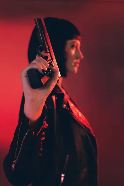 Woman with gun dressed in black against red background.