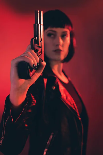Woman with gun dressed in black against red background. — Stock Photo, Image