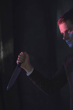 Elinde bıçakla kahverengi kazaklı genç adam.