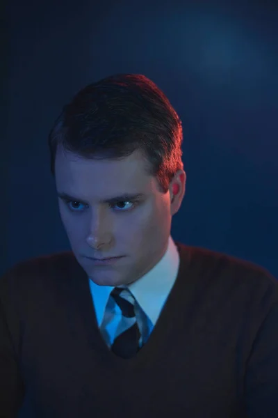 Serious man in tie and brown sweater. Lit by red and blue light. — Stock Photo, Image