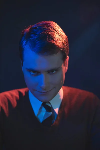 Homem sorrindo assustador de gravata e camisola marrom. Lit por vermelho e azul — Fotografia de Stock