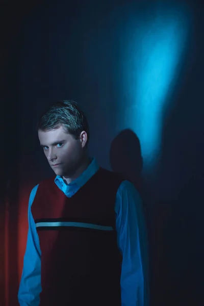 Man in het shirt en rode spencer in blauw en rood licht staande door w — Stockfoto