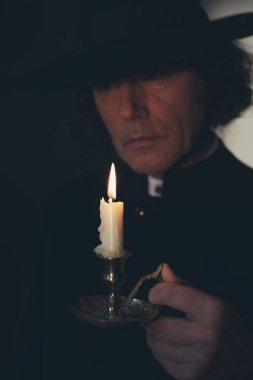 Siyah ceket ve şapka tutan mum gizemli Victorian rahip