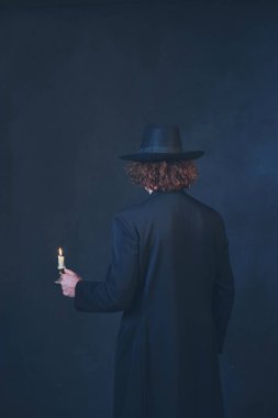 Siyah ceket ve şapka tutan gizemli adam mum. Arka v