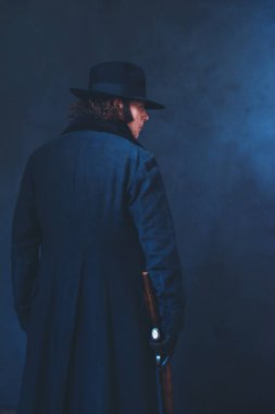 Uzun siyah ceket ve şapka tutan tüfekli Victorian adam. Arka Vie