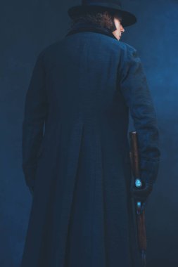 Uzun siyah ceket ve şapka tutan tüfekli Victorian adam. Arka Vie