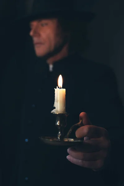 Mysterious victorian priest in black coat and hat holding candle — Stock Photo, Image